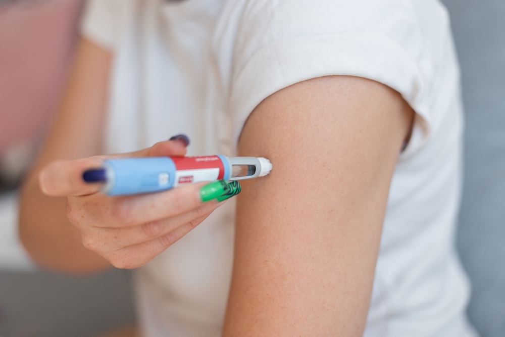 Person self-injecting Ozempic or Mounjaro into upper arm for weight loss treatment.