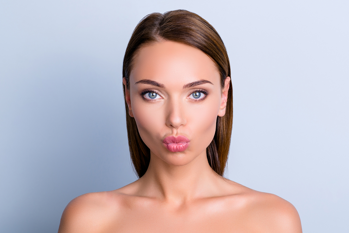 Woman with smooth, plump lips making a pout face after receiving lip filler treatment for enhanced volume and shape.