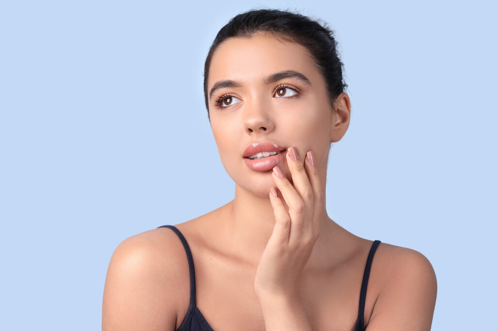 Woman gently touching lips with glowing skin, representing post-lip filler care using cold compress technique.