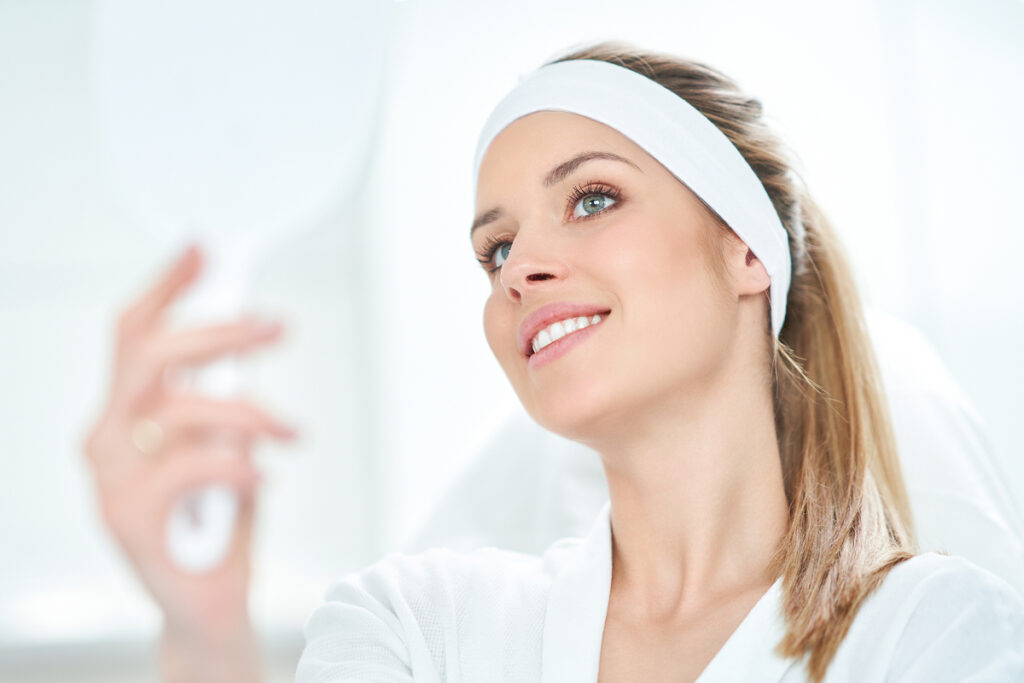 Smiling woman with clear skin pointing to cheek, representing safe skincare options during pregnancy.