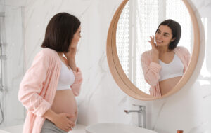 Pregnant woman in pink robe touching face and looking in mirror, considering Botox safety during pregnancy.