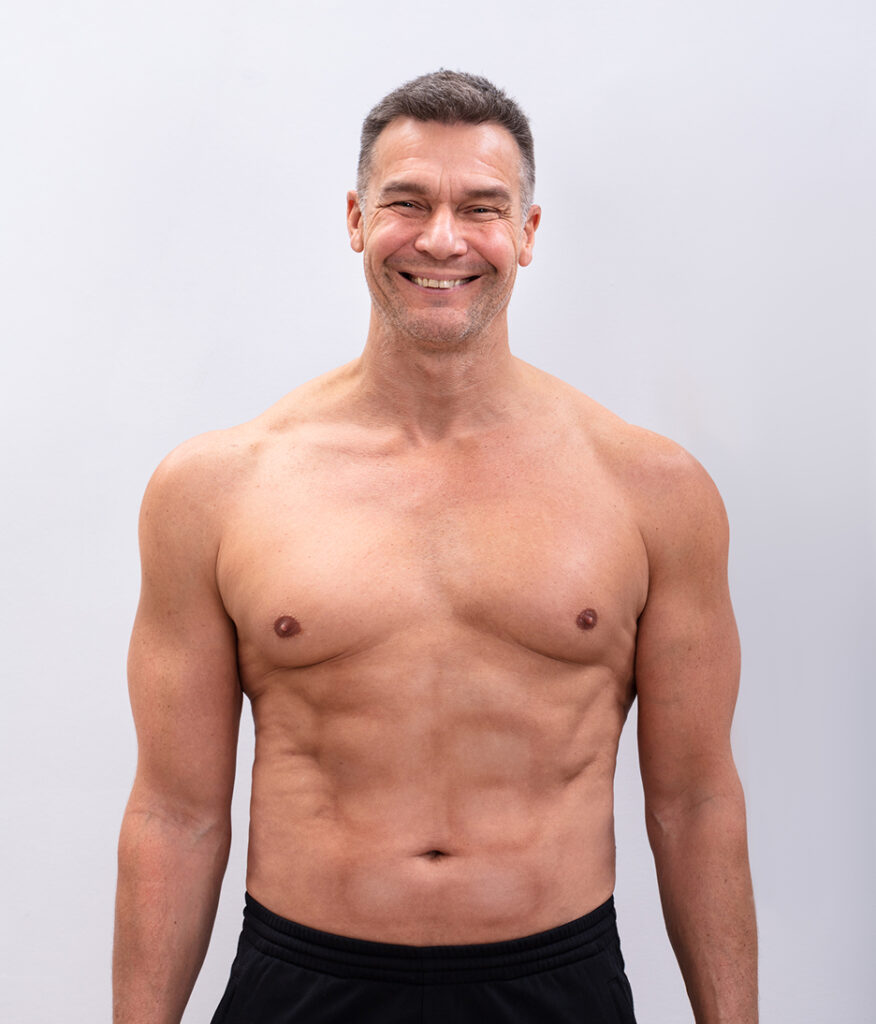 Healthy older man with defined muscles smiling confidently, representing safe Emsculpt NEO results for aging adults.