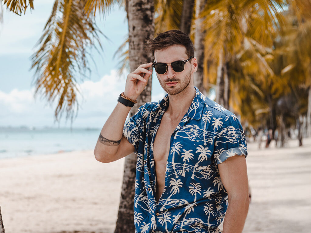 Confident man on tropical beach in sunglasses, representing health, vitality, and personalized executive wellness care.