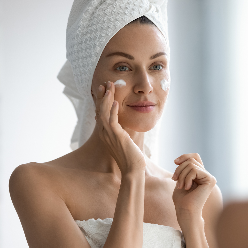 Woman applying cream with a towel on her head, showing gentle skincare practices after Botox treatment