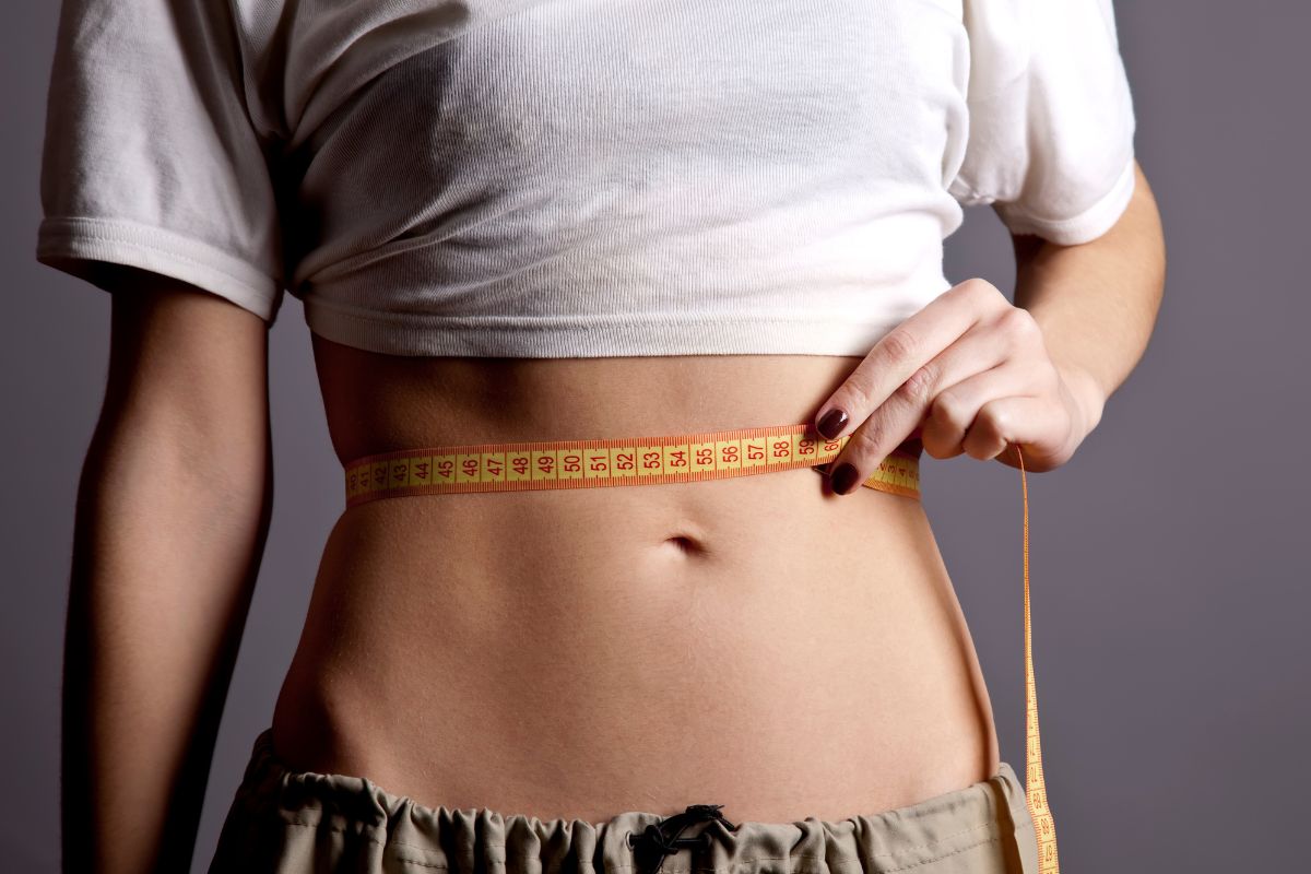 Woman measuring her slim waistline with a tape measure after choosing non-surgical body contouring over liposuction.