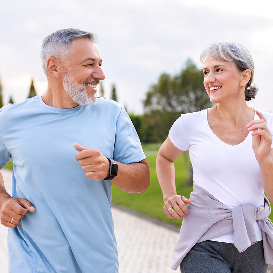 Smiling older couple jogging outdoors, representing improved vitality and aging through hormone optimization therapy.