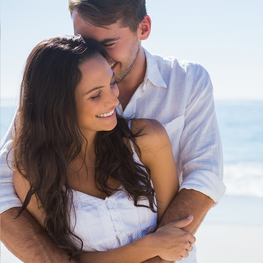 Smiling couple embracing at the beach, showcasing confidence and healthy hair after microneedling scalp therapy