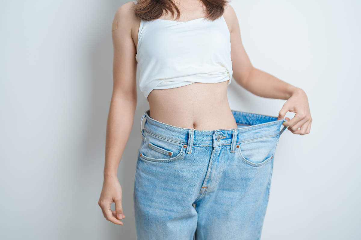 Woman in oversized jeans showing early weight loss progress after starting Ozempic treatment for appetite control.