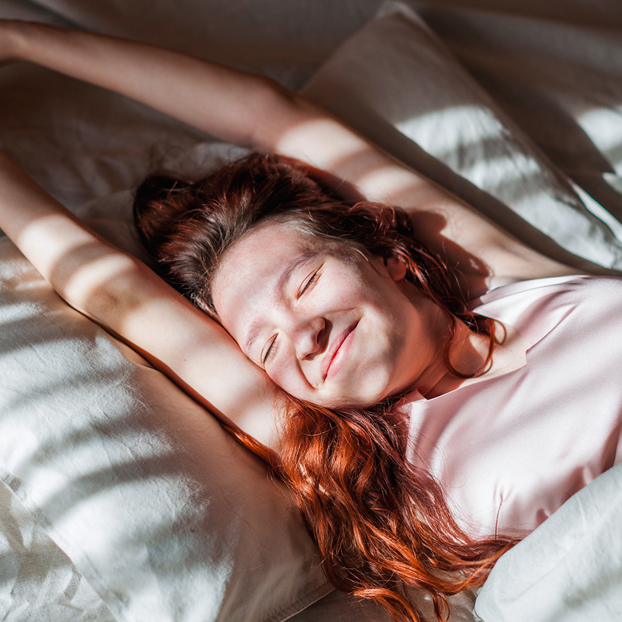 Relaxed woman stretching in morning light, representing improved sleep quality with peptide therapy support