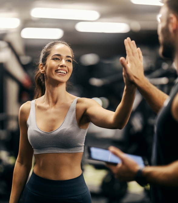 Smiling woman high-fiving trainer in gym, symbolizing successful post-Ozempic weight management at BODYWELLE Miami Beach.