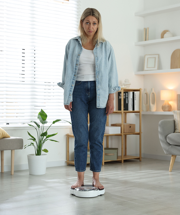 Middle-aged woman standing on a bathroom scale, looking concerned, symbolizing weight gain after stopping GLP-1 medication