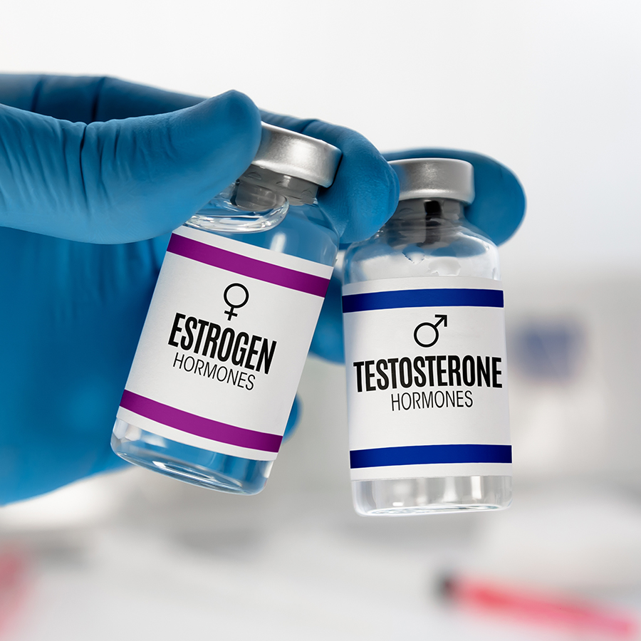 Gloved hand holding vials labeled estrogen and testosterone hormones for bioidentical hormone therapy treatment