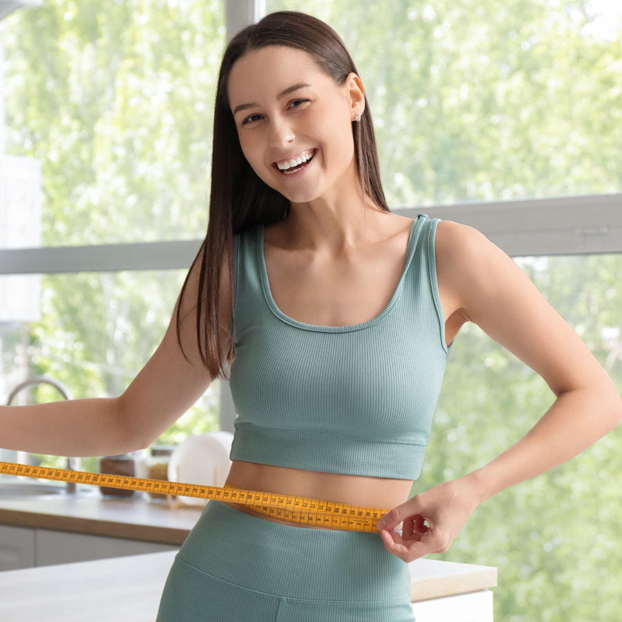 Smiling woman in fitness outfit measuring waist, representing successful weight loss results with Ozempic treatment