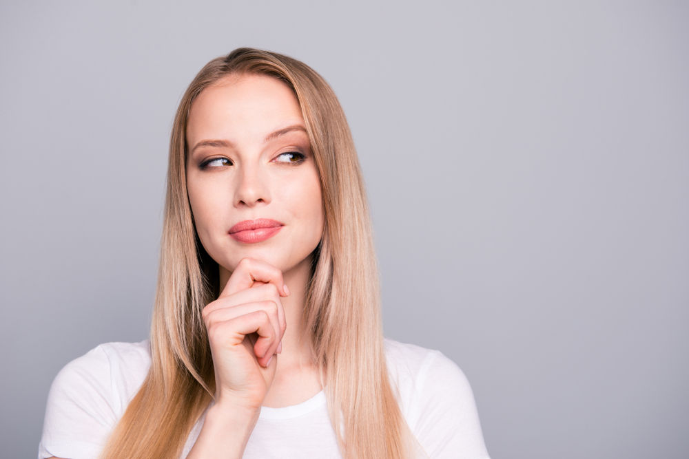 Thoughtful woman touching her face, representing how facial muscle activity affects Botox effectiveness and duration.