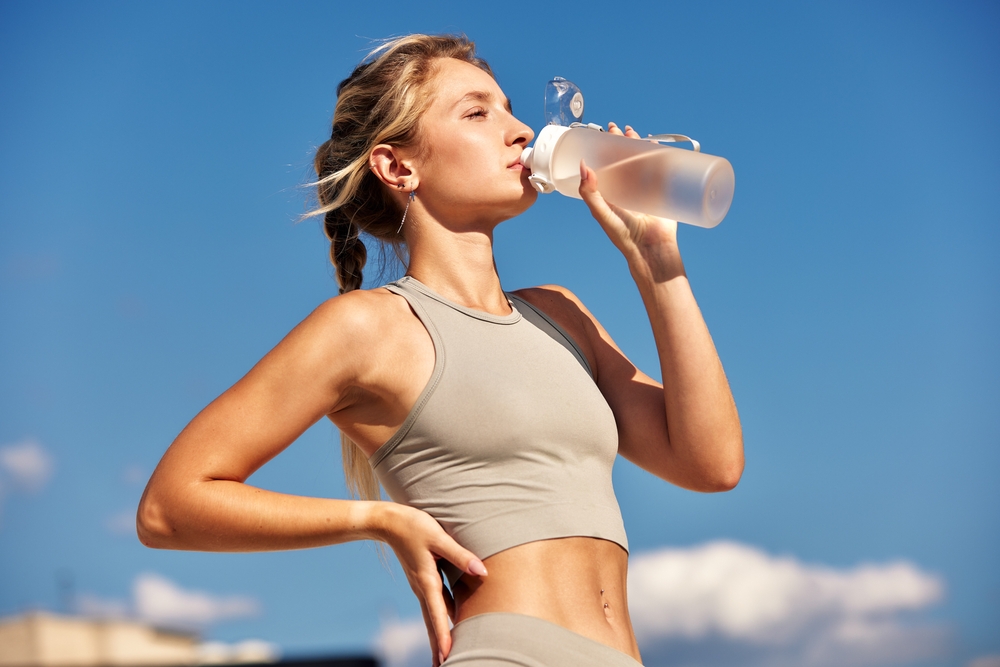 Fit woman in athletic wear drinking water outdoors, illustrating how high metabolism impacts Botox duration.