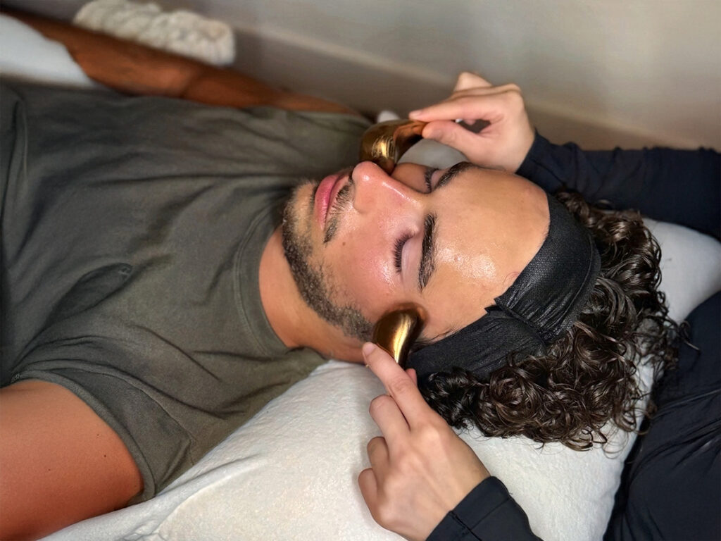 Man receiving a facial massage with golden tools during a personalized skincare session at BODYWELLE spa.