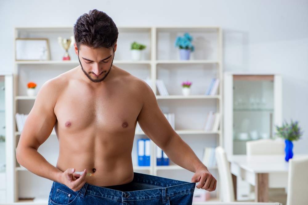 Shirtless man looking down at loose jeans, showing significant weight loss after using GLP-1 injections like Ozempic.