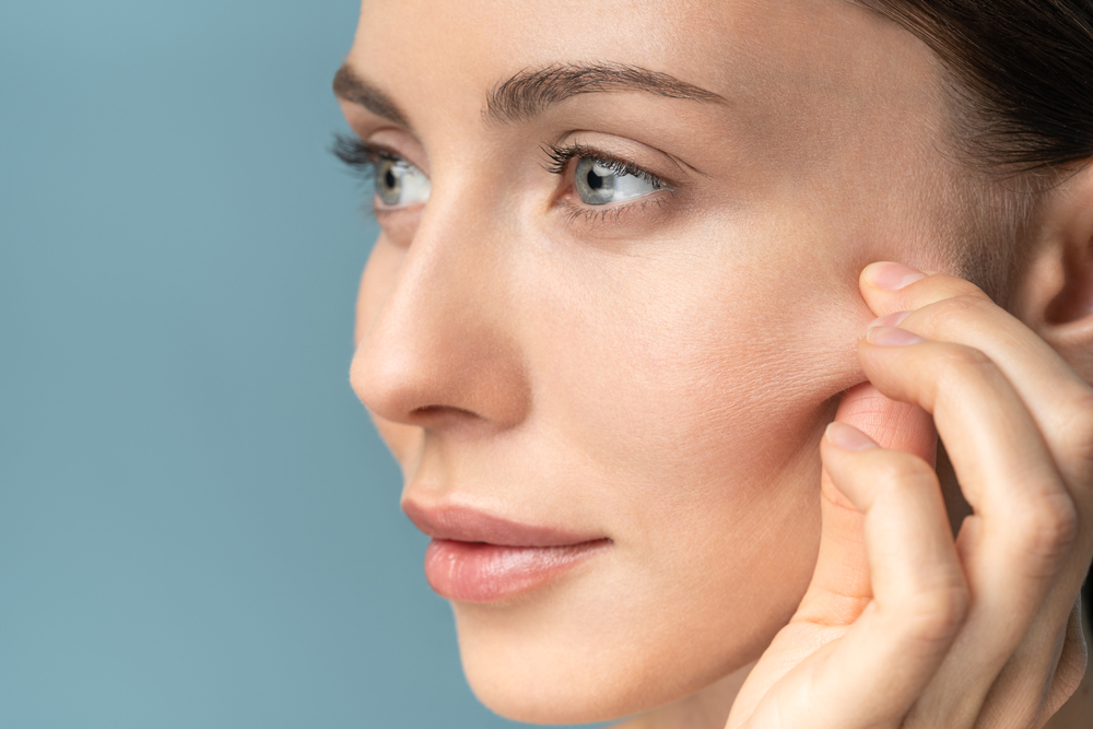 Close-up of woman gently pulling facial skin to show texture before Morpheus8 RF microneedling skin tightening treatment.