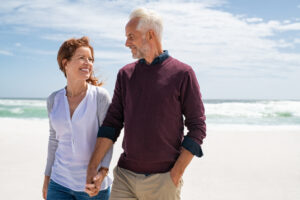 Smiling mature couple walking on the beach, representing the benefits of GLP-1 therapy for healthy aging and vitality.