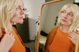 Woman examining her skin in the mirror, highlighting internal hydration benefits of Beauty IV therapy over topical creams.