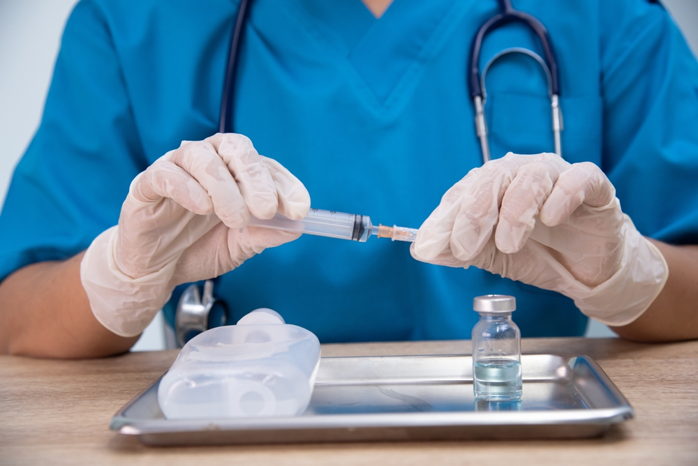 Medical professional in blue scrubs preparing Energy IV infusion with syringe and vial on a tray in clinical setting.
