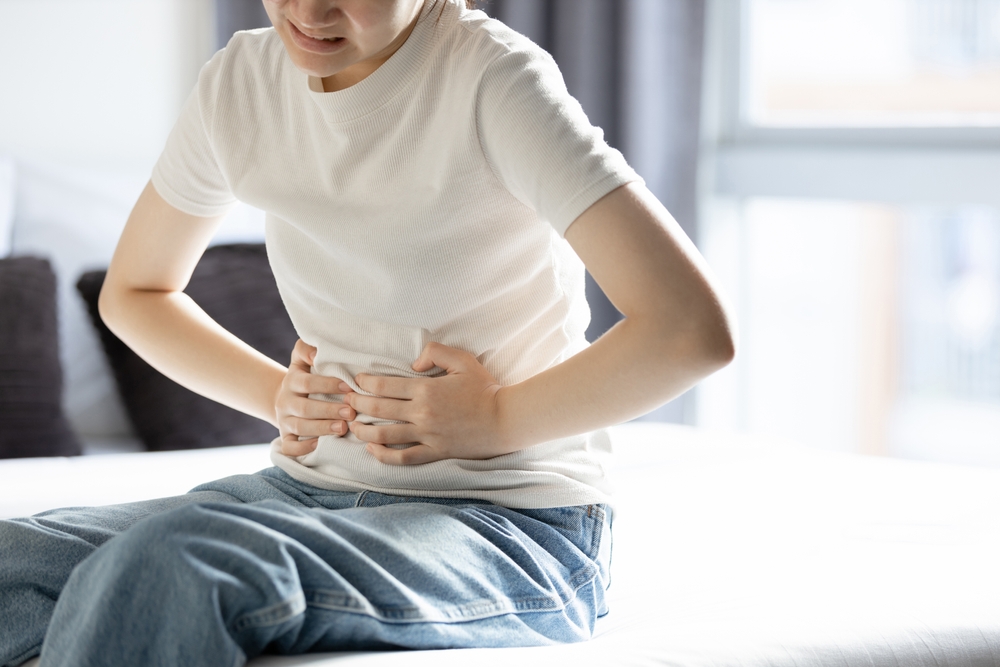 Person sitting on a bed holding their stomach, illustrating gastrointestinal side effects like nausea or abdominal pain from retatrutide.