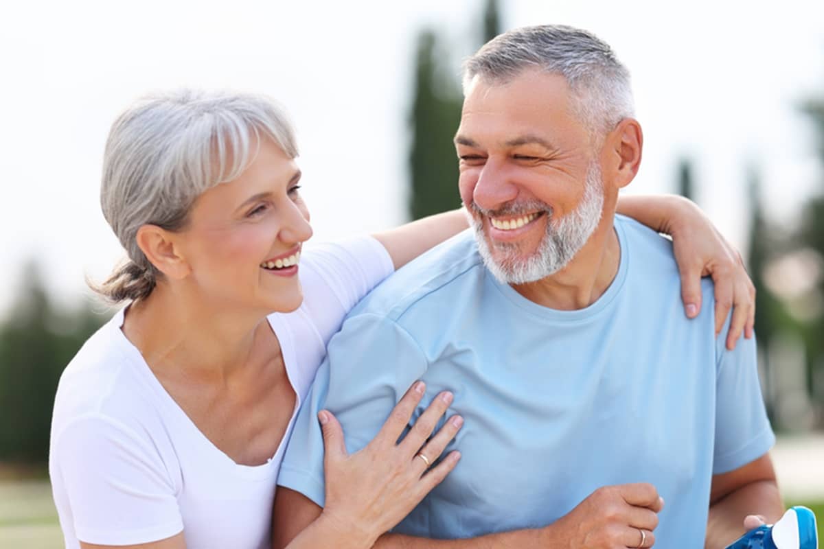 A happy, active senior couple with grey hair smiling and embracing outdoors, representing high vitality and a low biological age.