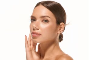 A young woman with radiant, smooth skin and a sleek hair bun posing with her hand gently touching her face to showcase clinical skin-tightening results.