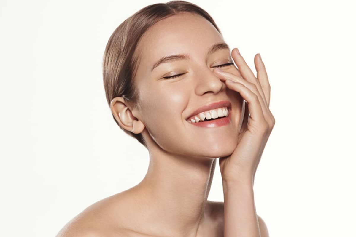 A young woman with glowing, clear skin laughing with her eyes closed and hand on her face, representing the results of successful skin resurfacing.