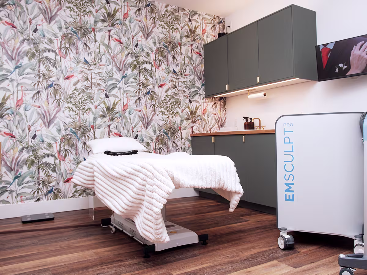 Treatment room with an EMSculpt NEO machine beside the exam table.