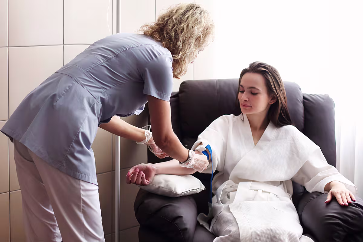 A healthcare professional wearing gloves prepares a seated patient's arm for an IV insertion.