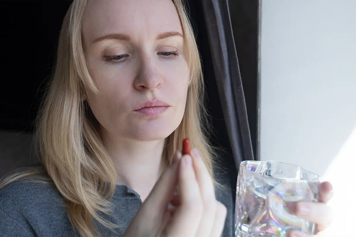 Woman holding an oral supplement with a glass of water.