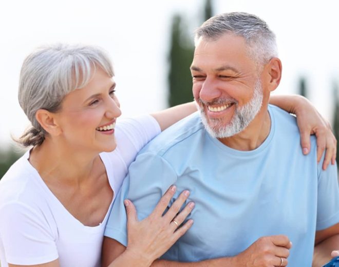 A happy, active senior couple with grey hair smiling and embracing outdoors, representing high vitality and a low biological age.