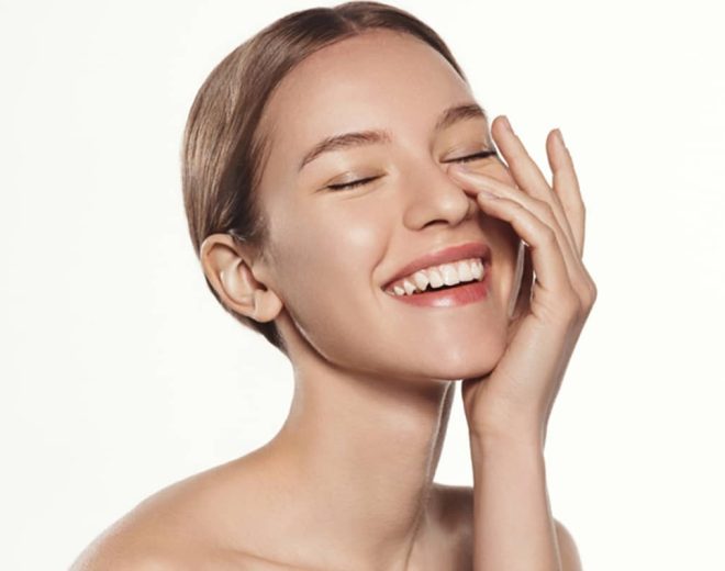 A young woman with glowing, clear skin laughing with her eyes closed and hand on her face, representing the results of successful skin resurfacing.